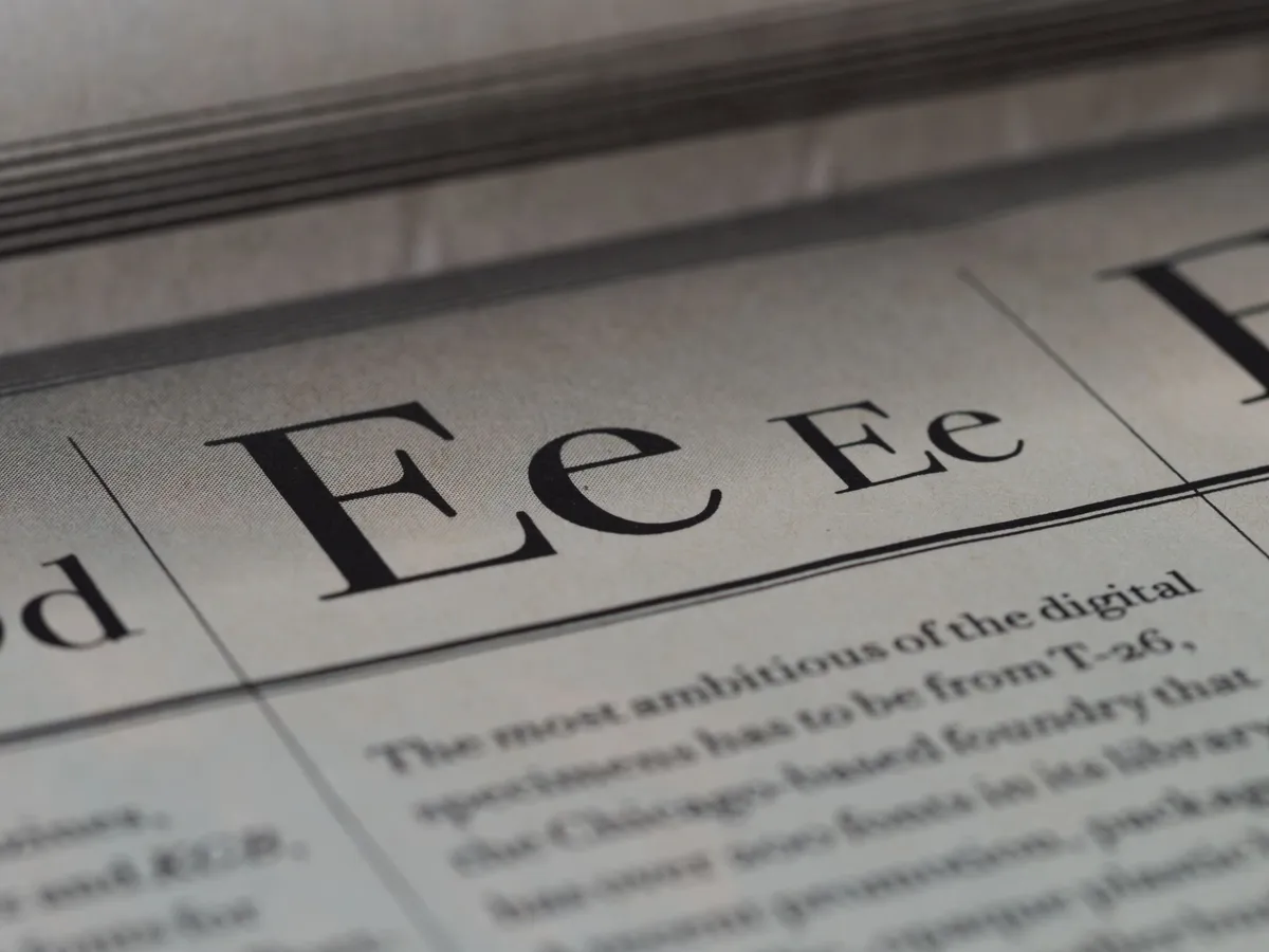 A printed type specimen page seen close up: a large serif capital and lowercase E ruled off from a column of body text, the page falling out of focus toward the spine.